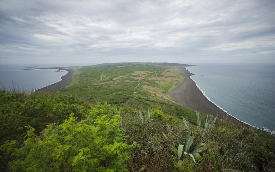 The view of Iwo To, historically known as Iwo Jima, from atop Mount Suribachi, includes the invasion beach to the right. To the left, shipwrecks in the distance remain near the beach. 
