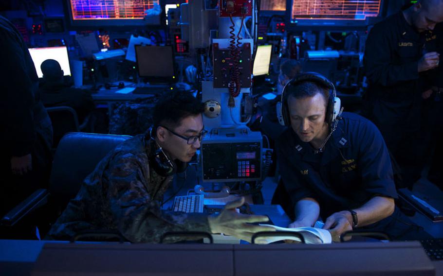 Lt. Richard Ray, right, from Thomasville, Georgia, discusses the Surface Ship Anti-Submarine Warfare Readiness and Effectiveness Measure exercise with Lt. Hyeoung Seok Noh, from Jeonju, Republic of Korea, in the combat information center aboard the USS John S. McCain in June 2014.