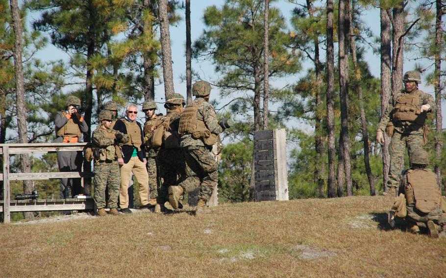 A mixed gender, two-person team of Marines carry a rocket launcher up a hill at Camp Lejeune, N.C., as Secretary of Defense Chuck Hagel looks on.