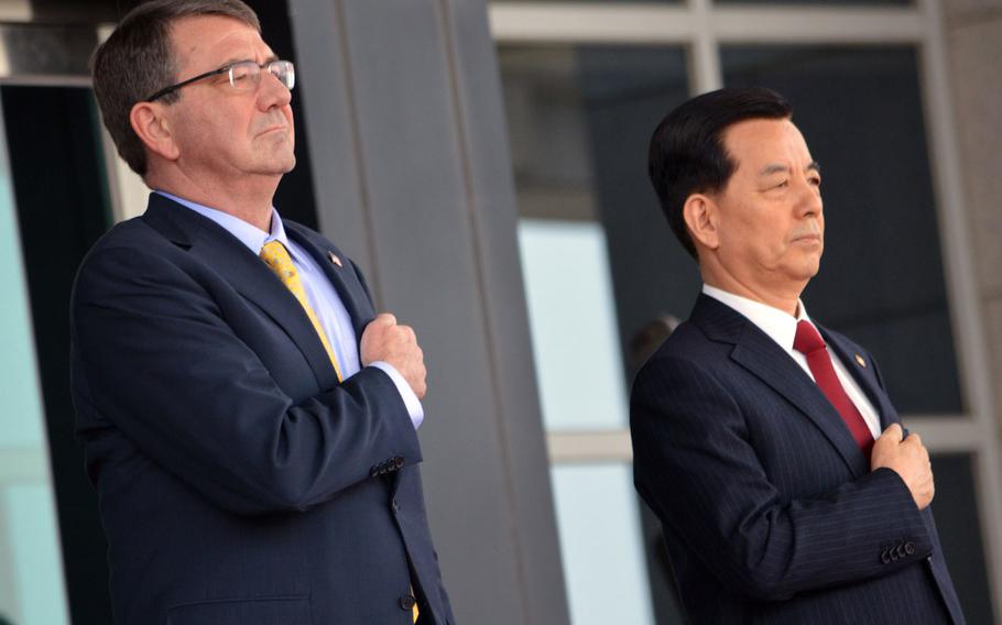 Defense Secretary Ash Carter, left, stands beside South Korean Defense Minister Han Minkoo during the playing of the national anthems at a ceremony at the Ministry of National Defense in Seoul on Friday, April 10, 2015. Carter gave a speech about defense of the Asia-Pacific region.