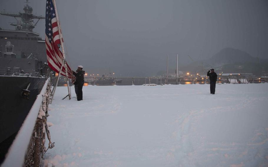 Sailors aboard the USS Ashland lower the flag during evening colors Sunday, Jan. 24, 2016, in Sasebo, Japan. Unusually heavy snowfall since Saturday has left some without running water and brought Sasebo Naval Base operations to a standstill, Navy officials said.