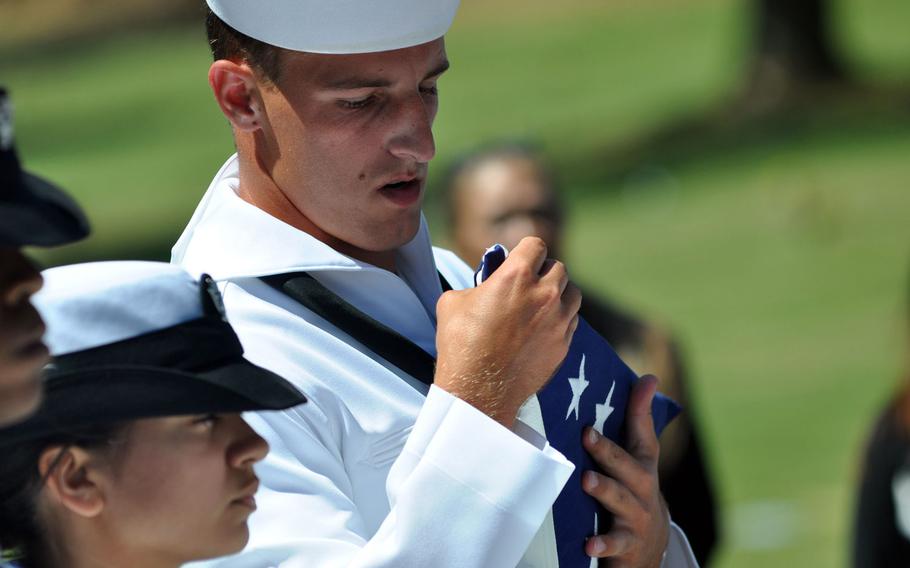 A sailor inspects the creases of the flag that had draped the casket of Petty Officer 1st Class Vernon T. Luke, a  USS Oklahoma crew member, during a funeral held March 9, 2016, at the National Memorial Cemetery of the Pacific in Honolulu.