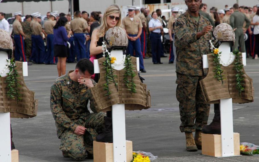 Mourners pause at crosses representing the 12 Marines who died in helicopter crashes Jan. 14, 2016, in Hawai. The crosses were adorned with flight gear, boots and Hawiian leis during a memorial Jan. 22, 2016, at Marine Corps Base Hawaii. Remains of nine of the Marines have been recovered.