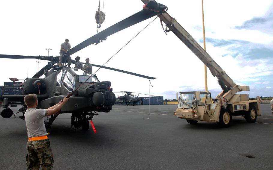 A soldier steadies a propeller on an Apache as a crew prepares it for flight after it had been stored for transport in a container ship from San Diego to Honolulu.