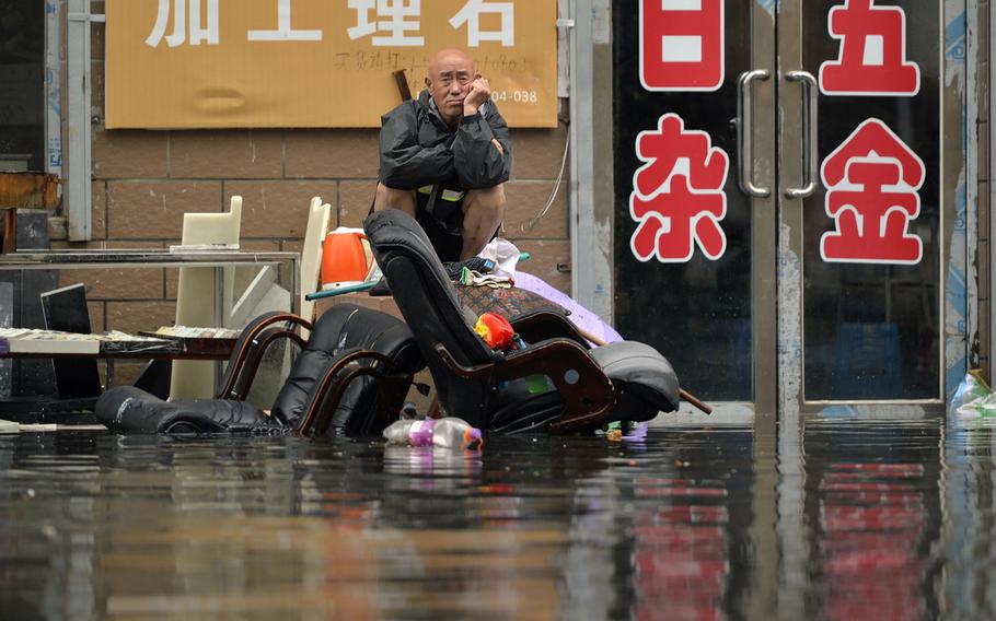 A man sits outside of a flooded shop in Shenyang in northeastern China's Liaoning Province on Thursday, July 21, 2016. Dozens of people have been killed and dozens more are missing across China after a round of torrential rains swept through the country earlier this week, flooding streams, triggering landslides and destroying houses. 