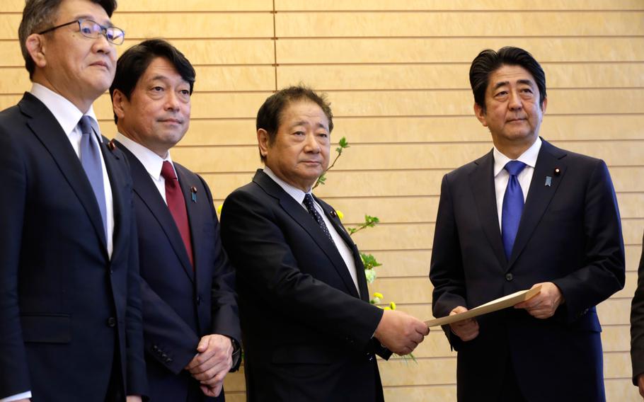 Hiroshi Imazu, second right, Chairman of Research Commission on Security of Japan's ruling Liberal Democratic Party (LDP) submits a proposal on missile defense to Japanese Prime Minister Shinzo Abe, right, flanked by former Defense Minister Itsunori Onodera, second left, head of LDP panel, at the prime minister's office in Tokyo, Thursday, March 30, 2017.