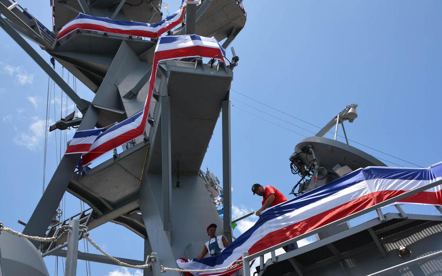 Workers unfurl bunting on the conning tower of the ship to be commissioned as the USS John Finn, Thursday, July 13, 2017.