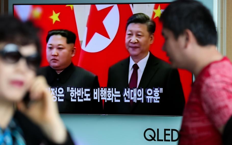 Pedestrians in Seoul, South Korea walk past a television screen showing a news broadcast, featuring North Korean Leader Kim Jong Un during a meeting with China’s president Xi Jinping on March 28, 2018.