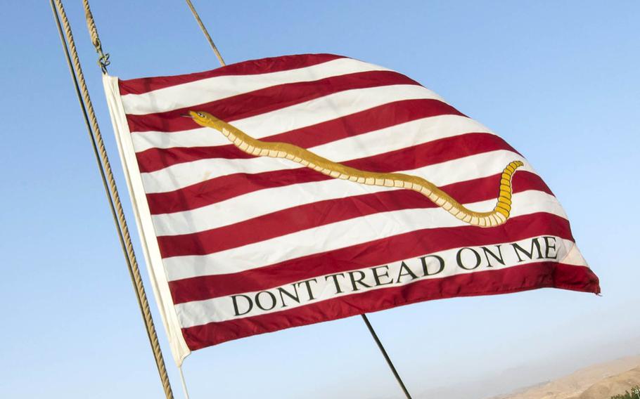 The First Navy Jack features a rattlesnake and the words “DON’T TREAD ON ME” on a red-and-white striped background.