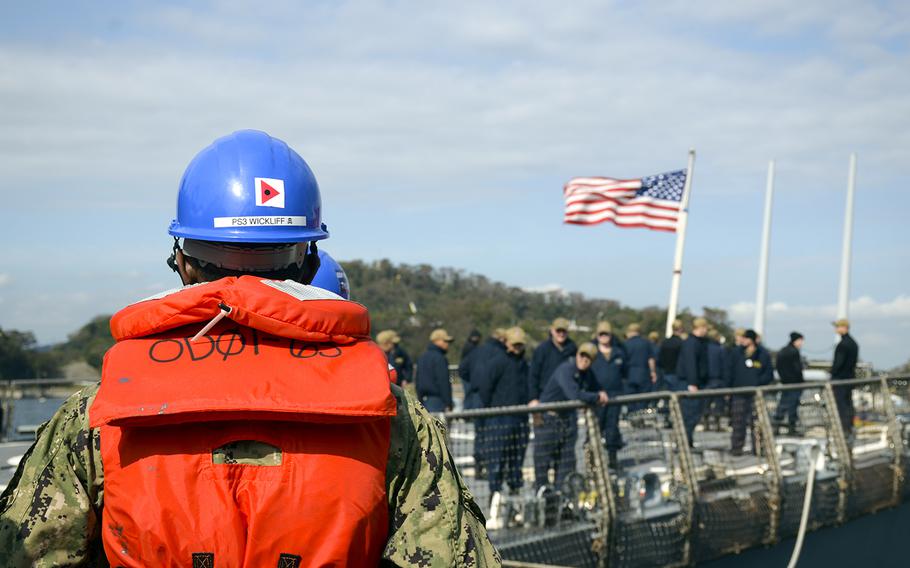 A sailor watches as the USS John S. McCain prepares to lower the flag from its stern and raise it on the mast to signify that it's officially underway at Yokosuka Naval Base, Japan. Monday, Oct. 28, 2019.