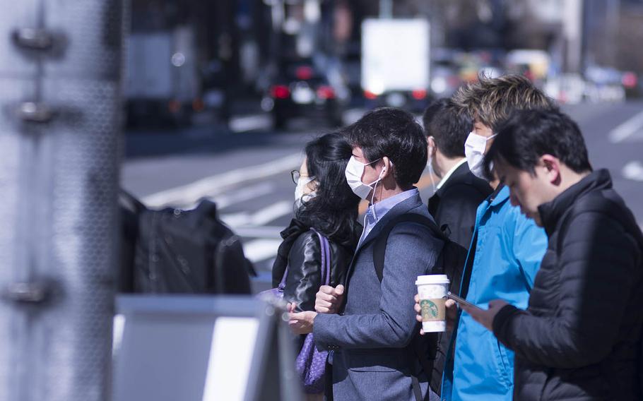 Pedestrians don masks to guard against illnesses such as the coronavirus in Tokyo, Thursday, March 12, 2020. 