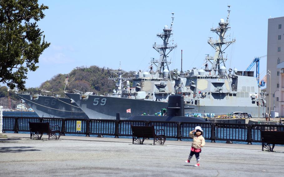 A child plays in a park across from the guided-missile destroyers USS. John S. McCain, left, and USS Russell at Yokosuka Naval Base, Japan, April 14, 2020. 