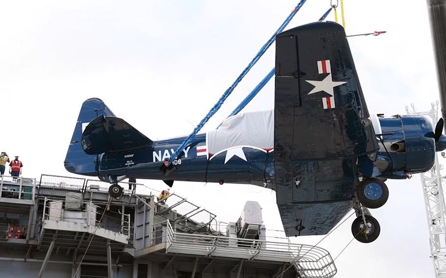 A World War II-era Navy plane is lowered by crane from the USS Essex onto a dock at Joint Base Pearl Harbor-Hickam, Hawaii, Aug. 11, 2020.