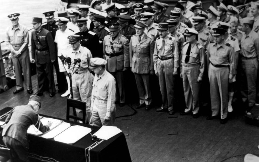 Gen. Douglas MacArthur and others watch as an Imperial Japan official signs a surrender document aboard the USS Missouri moored in Tokyo Bay, Sept. 2, 1945.