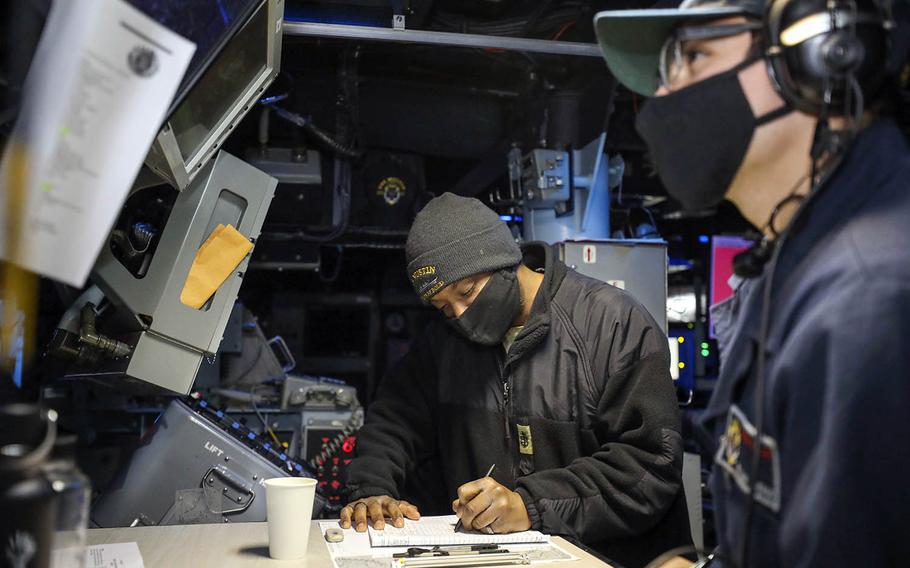 Chief Dayshawn Davis, of Catawba, N.C., and Seaman Apprentice William Viveros, of Fort Worth, Texas, maintain logs in the combat room as the guided-missile destroyer USS Mustin sails in the East China Sea, Dec. 18, 2020. 