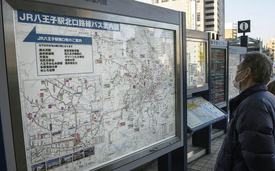 A masked visitor scans a map outside the train station in Hachioji, Japan, Feb. 2, 2021. 