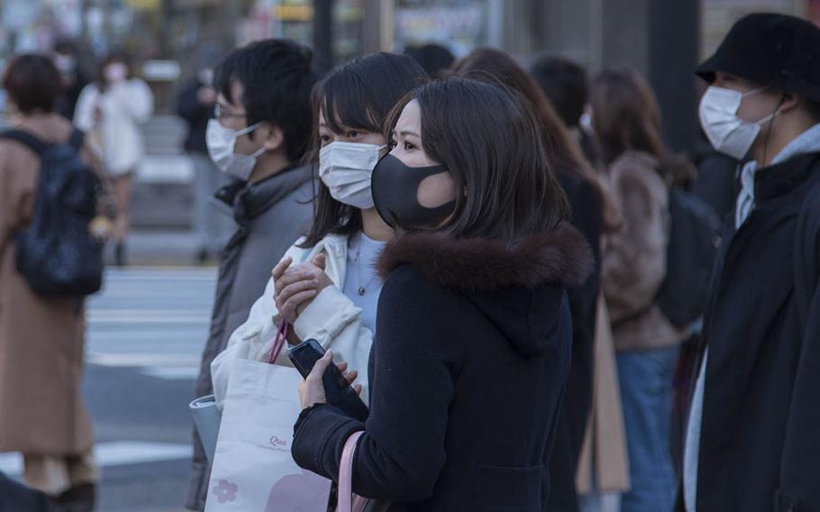 Pedestrians wearing masks as protection against the coronavirus wait to cross a street in central Tokyo, Feb. 4, 2021.