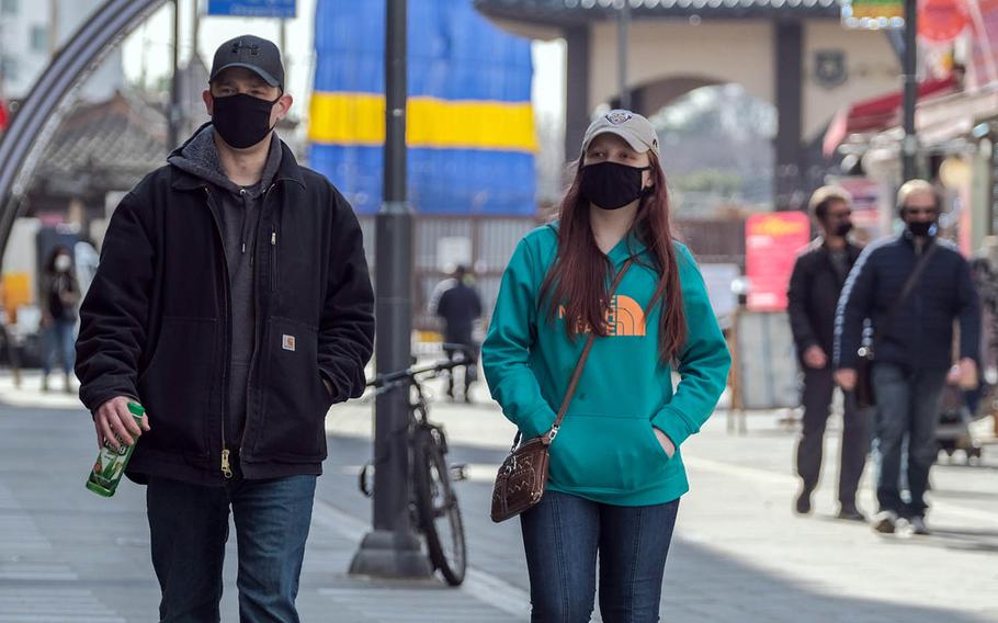 People wear masks while strolling through the Songtan entertainment district outside Osan Air Base, South Korea, Tuesday, March 2, 2021.