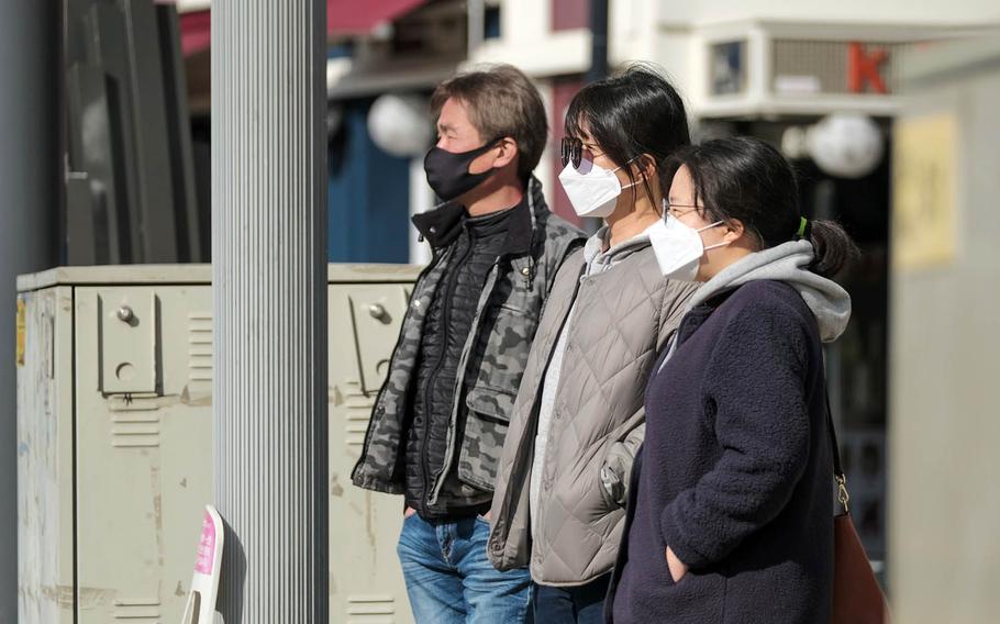 People wait to cross a busy intersection outside Osan Air Base, South Korea, March 2, 2021.
