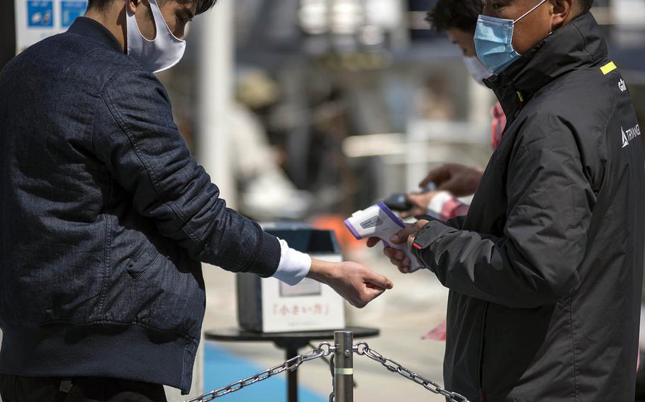 A man wearing a mask as protection against the coronavirus has his tempertature checked, another pandemic precaution, in Yokosuka, Japan, March 19, 2021. 