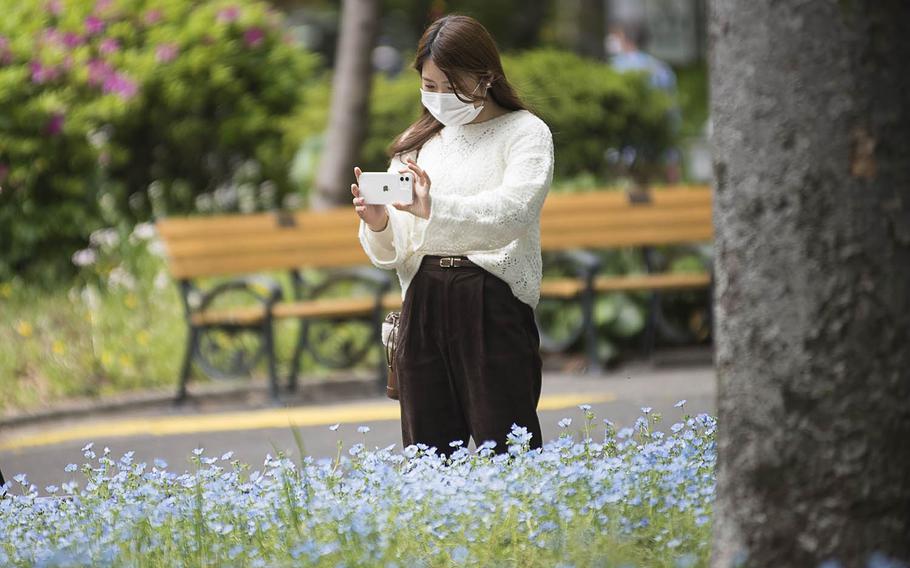 A woman wears a mask while snapping photos of spring flowers at Hibiya Park in central Tokyo, April 13, 2021. 