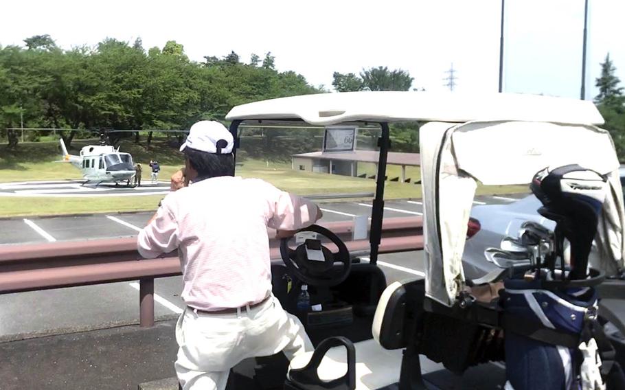 A golfer watches a UH-1N Iroquois helicopter land near the golf course at Tama Hills Recreation Area in western Tokyo, Saturday, May 1, 2021.