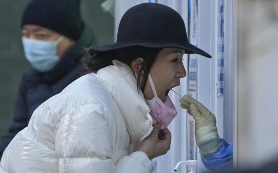A woman has her routine COVID-19 throat swab at a coronavirus testing site in Beijing, Sunday, Dec. 4, 2022. China on Sunday reported two additional deaths from COVID-19 as some cities move cautiously to ease anti-pandemic restrictions amid increasingly vocal public frustration over the measures. 