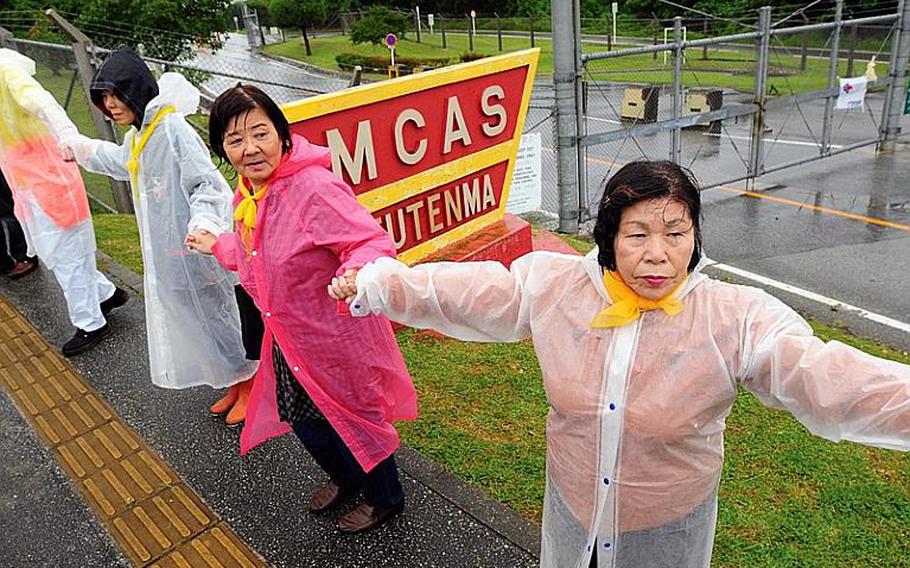 A few of the thousands of anti-base protesters at Marine Corps Air Station Futenma hold hands in front of the base sign during a demonstration last month, symbolically closing the controversial base.