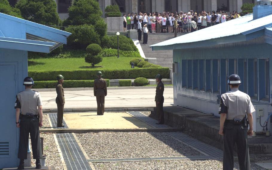 Soldiers from North Korea and South Korea stand yards apart on opposite sides of the Military Demarcation Line at the Joint Security Area of the Demilitarized Zone on Thursday as a tour group looks on from the North Korea side.