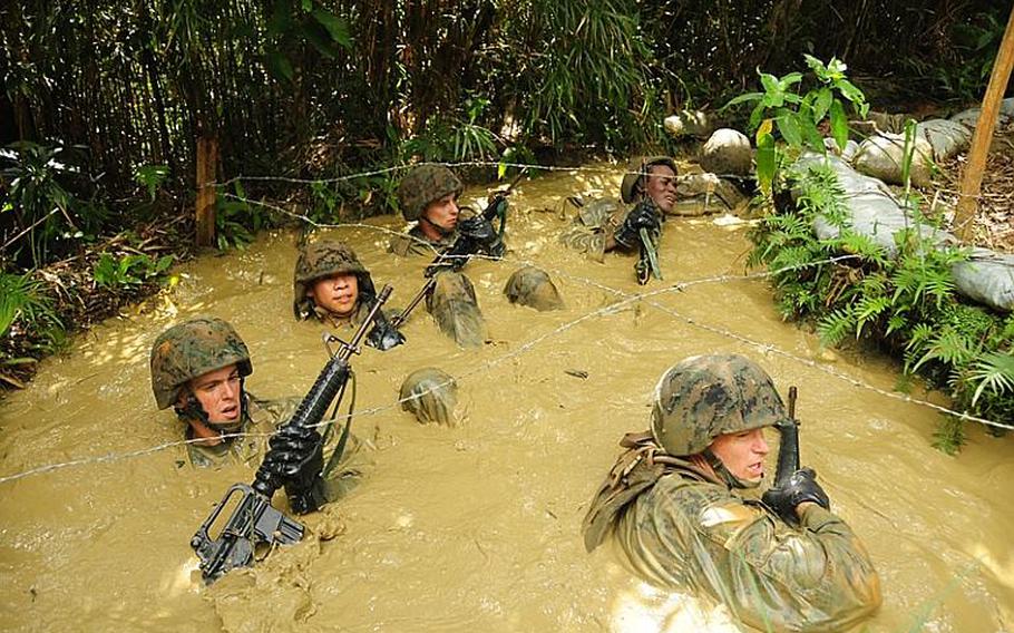 Troops struggle to navigate through the barbed wire that is strung just above the water's surface. The Marines' uniforms and rifles are easily snagged on the wire, so they navigate the water obstacles on their backs.