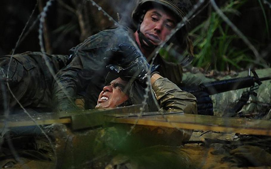A Marine drags another underneath a Plexiglas obstacle. If the Plexiglas falls, all the Marines on the team must do the water obstacle again.