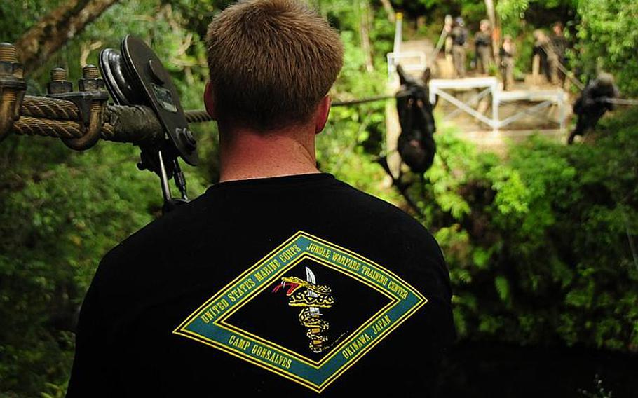 A Jungle Warfare Training Center instructor looks on as Marines cross a ravine on a heavy gauge wire. The Marines are secured to the wire in case they fall. If they fall, the instructor will slide over via a pulley and attach a rope to the  Marine. Troops from the fallen Marine's team will then pull their teammate to the other side.