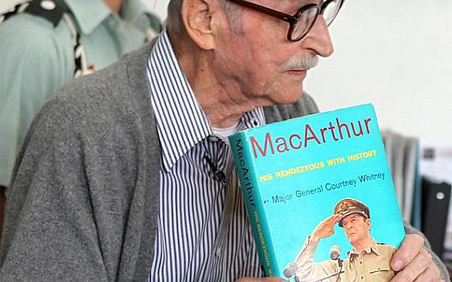 Mike Jurkoic, a retired World War II veteran who once stepped in an elevator with the famous Gen. Douglas MacArthur, shows the students at Zama American High School a copy of a book about MacArthur that he had signed by the author, Maj. Gen. Courtney Whitney.