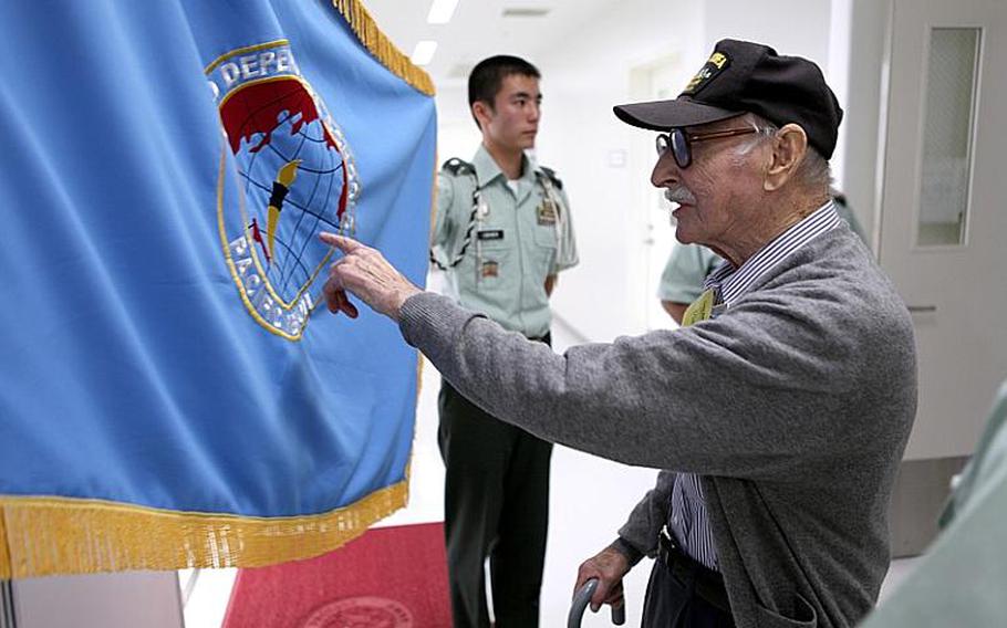 World War II veteran Mike Jurkoic looks at the flag representing the Department of Defense Dependents Schools during his visit Tuesday to Zama American High School.