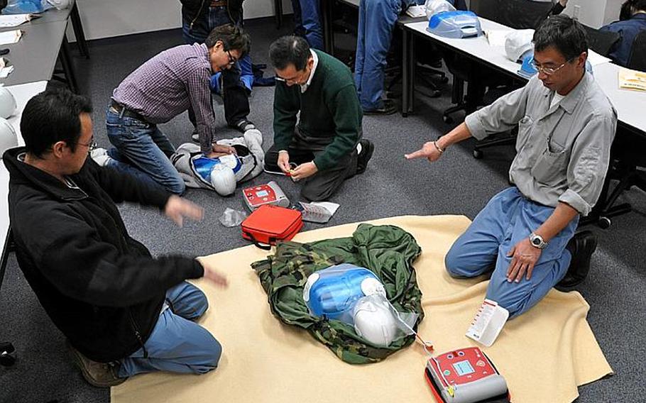 Jun Sasaki, left, and Yasuo Urushizawa, right, lift their hands away from a training dummy prior to giving it a simulated shot with an automated external defibrillator during a training session Tuesday at Misawa Air Base, Japan. Members of the Japanese Red Cross Society came to the base to provide the training to Japanese employees who work with the U.S. Air Force's 35th Civil Engineer Squadron.