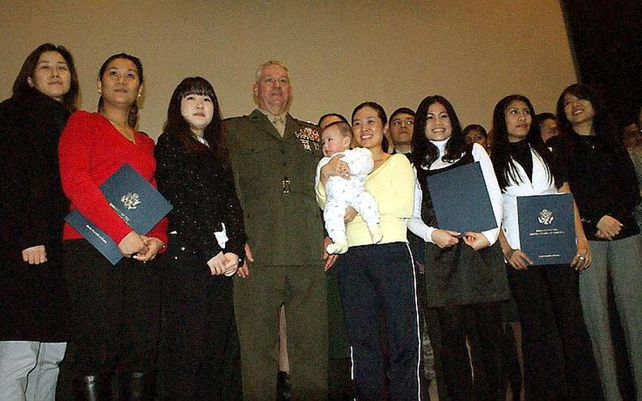 Marine Maj. Gen. Mark Gurganus, commander, U.S. Marine Corps Forces Korea, poses on stage with newly sworn-in U.S. citizens, including five-month-old Ryan Huang, during a naturalization ceremony Wednesday at Yongsan Garrison, South Korea.
