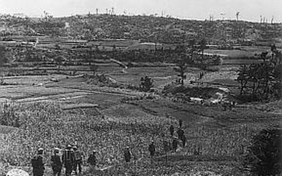 A column of soldiers from the 3rd Battalion, 382nd Regiment snake toward the first Japanese defensive line on April 20, 1945. They are using packboards to move ammunition, rations and water to attacking troops.