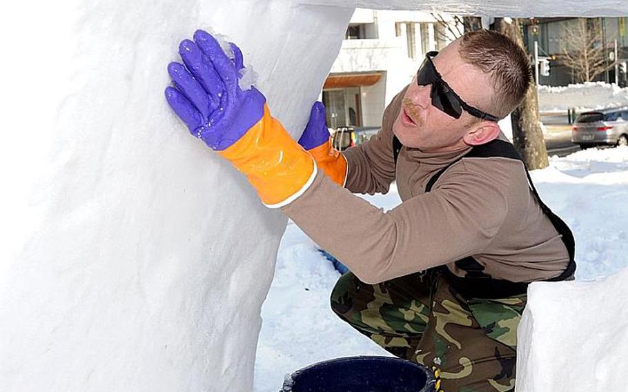 Navy Chief Petty Officer Billy Knox applies wet handfuls of snow to the base of a snow sculpture Thursday to try to reinforce it as it slowly melted in unseasonably warm conditions during the Sapporo Snow Festival. Knox is leading a five-member team of U.S. sailors from Misawa Air Base, Japan, who were invited to the 62nd annual festival to represent the U.S. Navy.