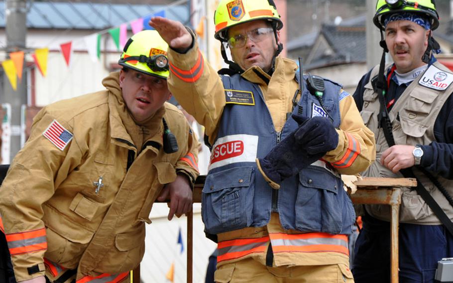 From left, Bob Zoldos, Mark Plunkett and Bobby Ritchie, members of a Fairfax, Va.-based search-and-rescue unit, gesture toward earthquake and tsunami damage on Tuesday morning in Ofunato, Japan.