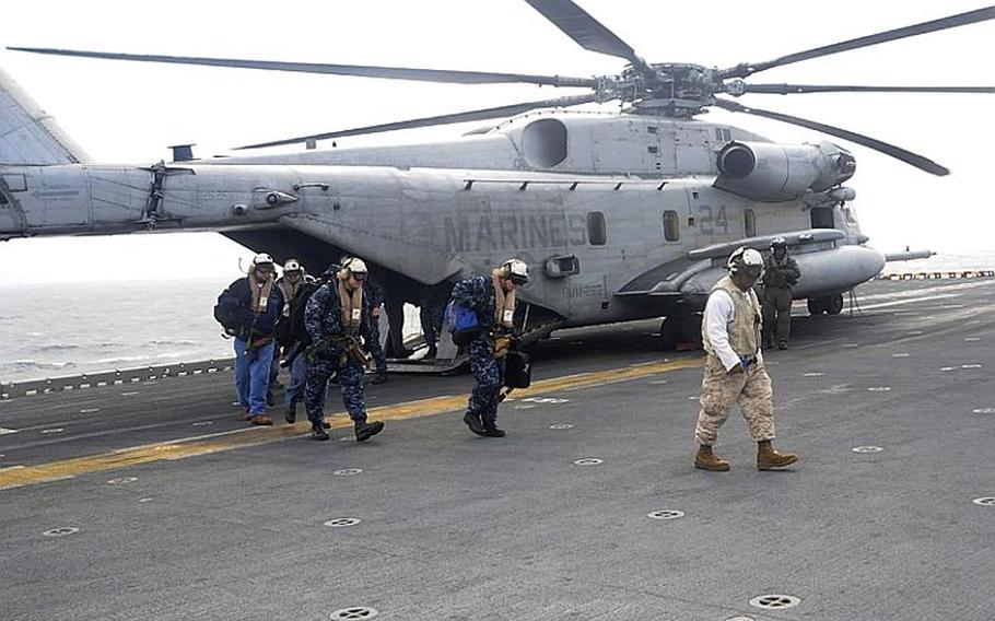 Members of a U.S. Navy radiological assistance team debark from a CH-53 Sea Stallion on the flight deck of the amphibious assault ship USS Essex. The 21-member team will check for radiation on personnel and aircraft who travel in areas affected by radiation from the Fukushima Daiichi nuclear plant.