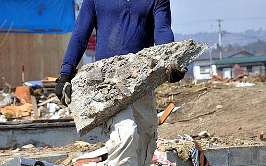 Civilian volunteer Alex Chamberlain, a member of the Misawa Air Base community, lugs a big chunk of concrete while helping clean the tsunami-ravaged Noda Village during a base-sponsored trip on Friday.
