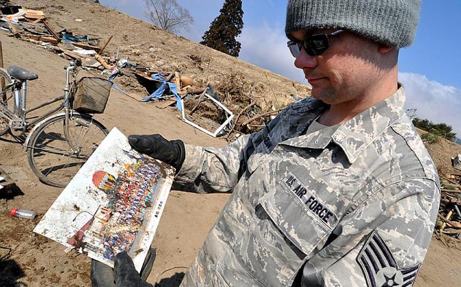 Staff Sgt. Chris Grogean, on temporary duty to Misawa Air Base, Japan, from Okinawa, reads the front of a picture discovered in the debris of Noda village on Friday. Grogean, who learned to speak Japanese while working as an English teacher previously in Japan, volunteered to serve as a translator on Friday's trip two hours down the coast from the base. In addition, a Japanese employee from the base volunteered Friday, making communication with village officials even easier.