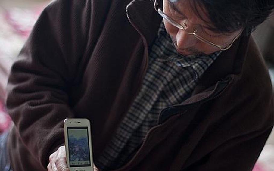 Hidetoshi Oikawa, a dental technician who now lives at the Kadonowaki Middle School shelter in Ishinomaki, Japan, shows photos he took of the March 11 tsunami destroying his home.
