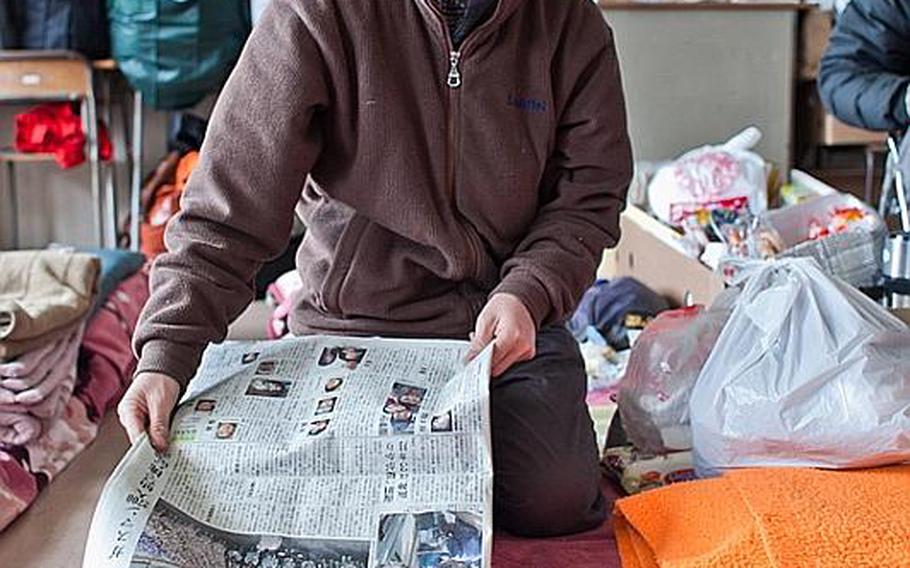 Hidetoshi Oikawa, a dental technician, who now lives at the Kadonowaki Middle School shelter in Ishinomaki, Japan, demonstrates, using an alarm clock as his home and the newspaper as the water, how the March 11 tsunami destroyed his home. 