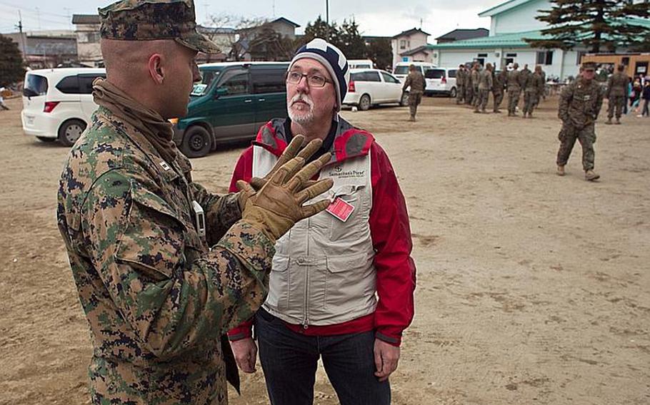Marine Corps Capt. Robert Gerbracht and Darren Polischuk, a Canadian worker with the Christian relief organization Samaritan's Purse chat after Marines helped deliver boxes of aid that Samaritan's Purse had provided to the displaced residents of the Watanoha Elementary School shelter in Ishinomaki, Japan. The U.S. military has been coordinating with other NGOs to deliver aid.