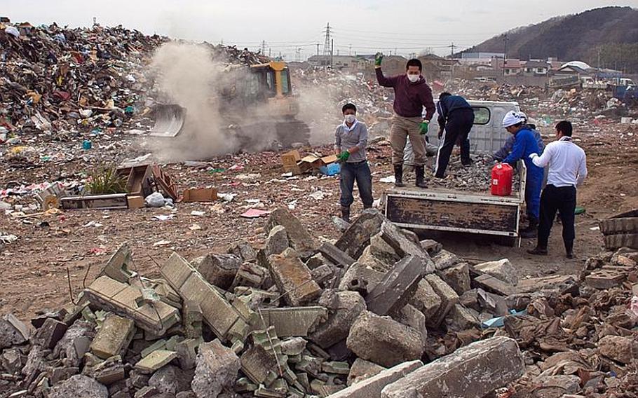 A group of locals empty their truck load of concrete debris as a city worker in a bulldozer moves to consolidate the scattered garbage at one of two massive dump sites set up to store tsunami-related trash in Ishinomaki, Japan.