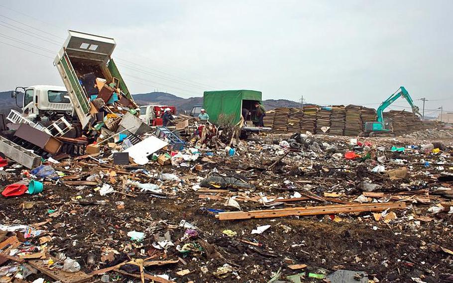 A mound of thousands of waterlogged tatami mats sit in the distance as people bring more garbage and city employees work to consolidate mounds of trash at one of two temporary tsunami-related trash dump sites in Ishinomaki, Japan.