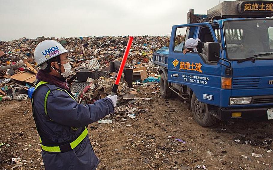 A city worker guides a truck full of tree limbs to the edge of one of two temporary tsunami-related trash dump sites in Ishinomaki, Japan.