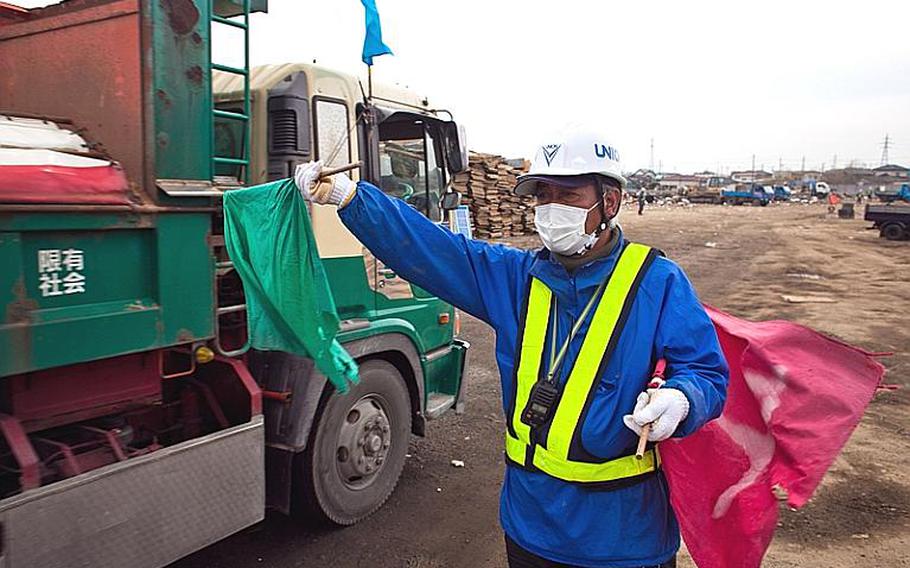 Watanabe Seichi, 55, a city worker, allows passage to a truck full of debris at one of two temporary tsunami-related trash dump sites in Ishinomaki, Japan.