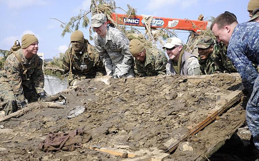 Army veteran Matt Szymanski, fifth from left with the U.S. flag patch on his hat, helps a group of Marines, airmen and sailors attempt to lift a giant piece of debris while helping clean Noda Village, about a two-hour drive from Misawa Air Base, Japan, during a March 29 trip. Szymanski flew to Japan at his own expense to help relief efforts in the Japanese community.